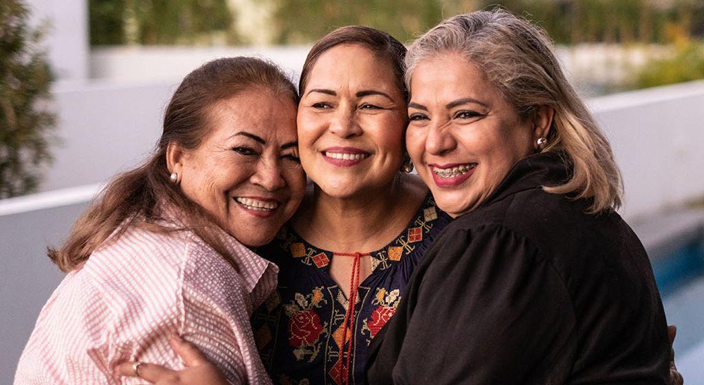 three woman smiling and hugging each other in support of each other's menopause stages 
