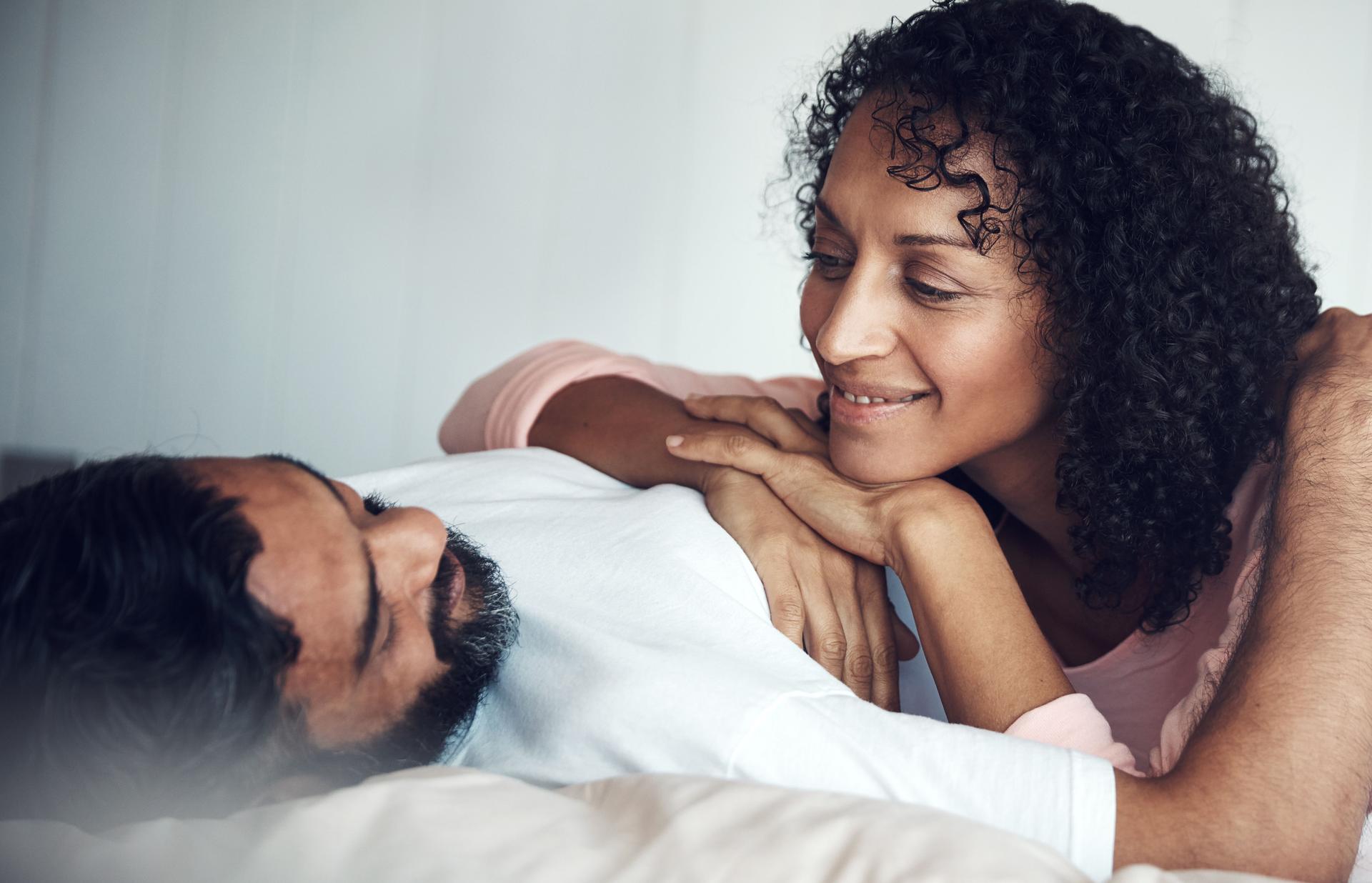 a couple laying in bed talking about how to increase their sex drive during menopause, discussing options of menopause hormone therapy or vaginal lubricants