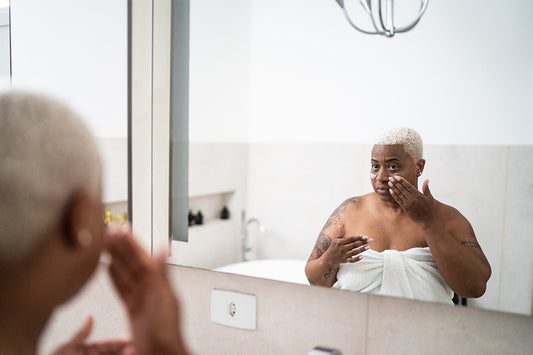 a woman applying an over-the-counter regimen in front of a mirror to treat her menopausal acne