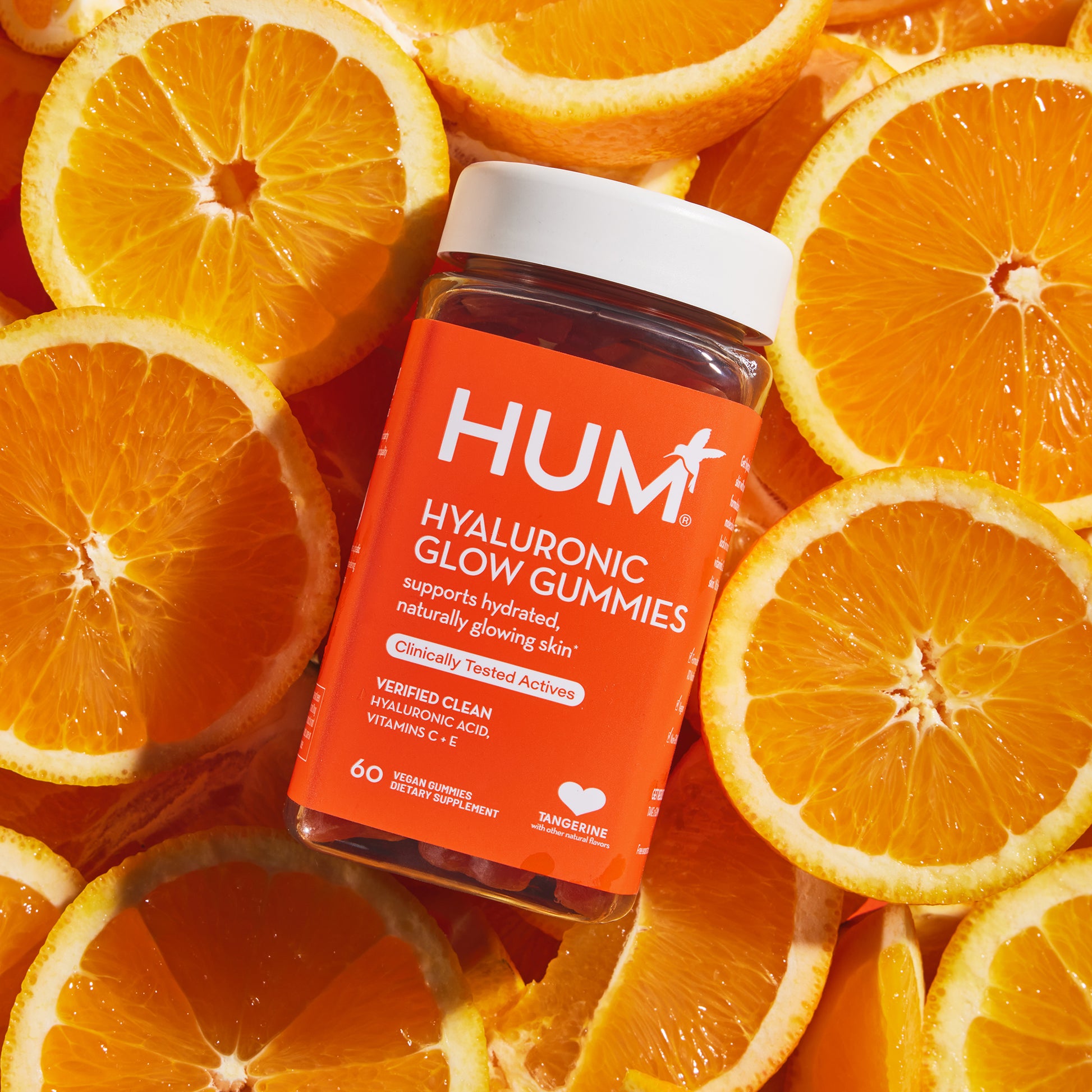 bottle of HUM NUTRITION Hyaluronic Glow gummies, surrounded by tangerine slices